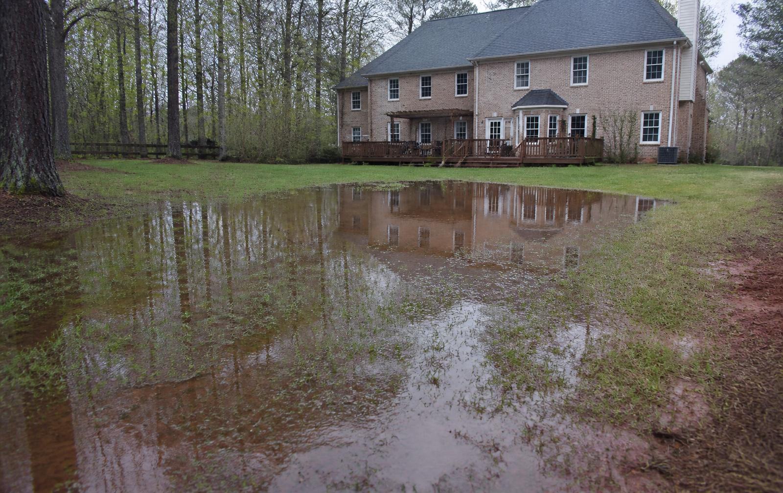 Standing water pooling across a soggy back lawn behind a brick home in metro Atlanta after heavy rain